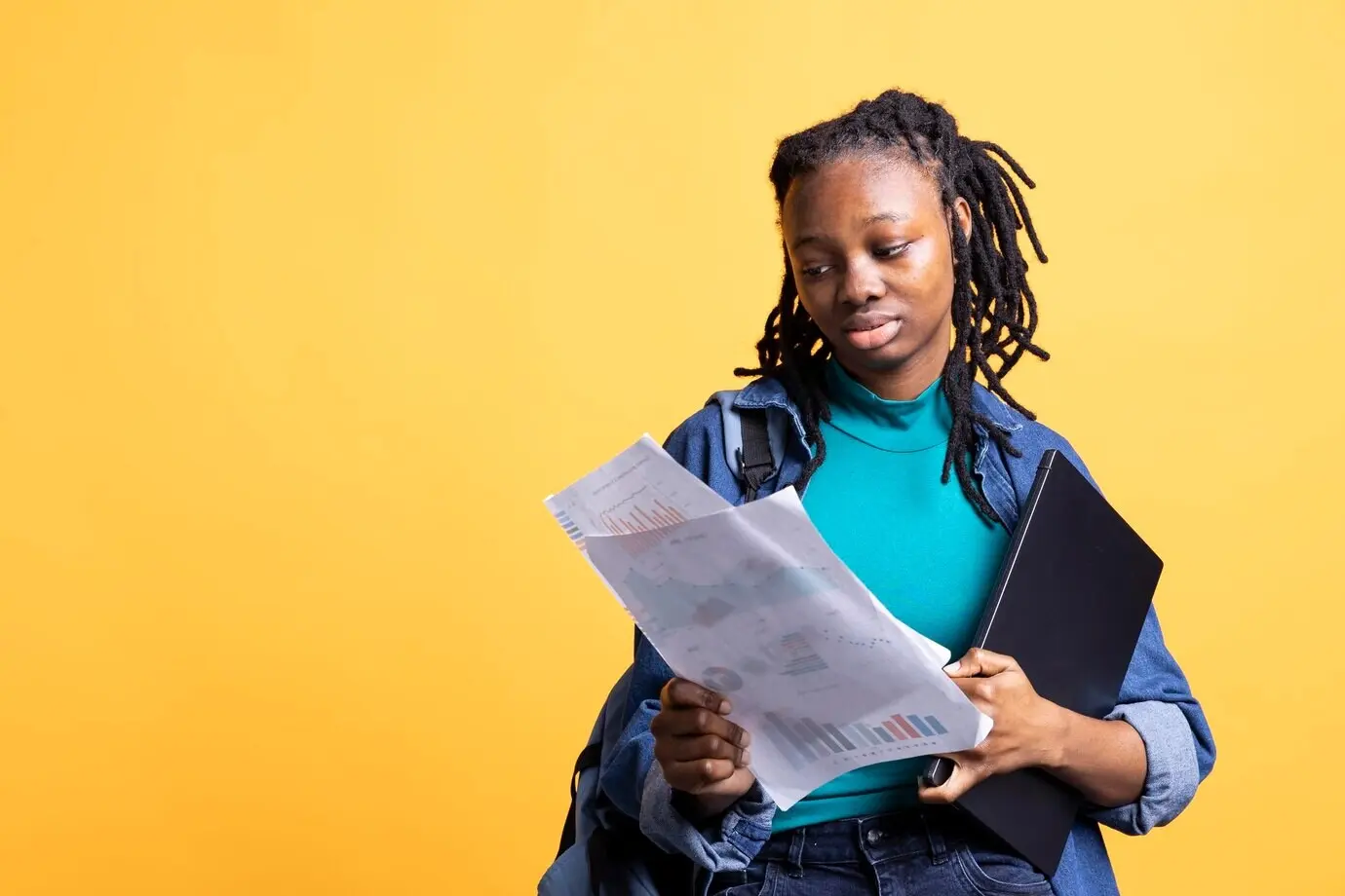 Молодая девушка читает документы с экономическими графиками на студийном фоне.